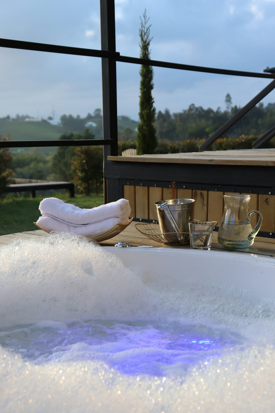 Outdoor hot tub with blue light and white bubbles on a deck.
