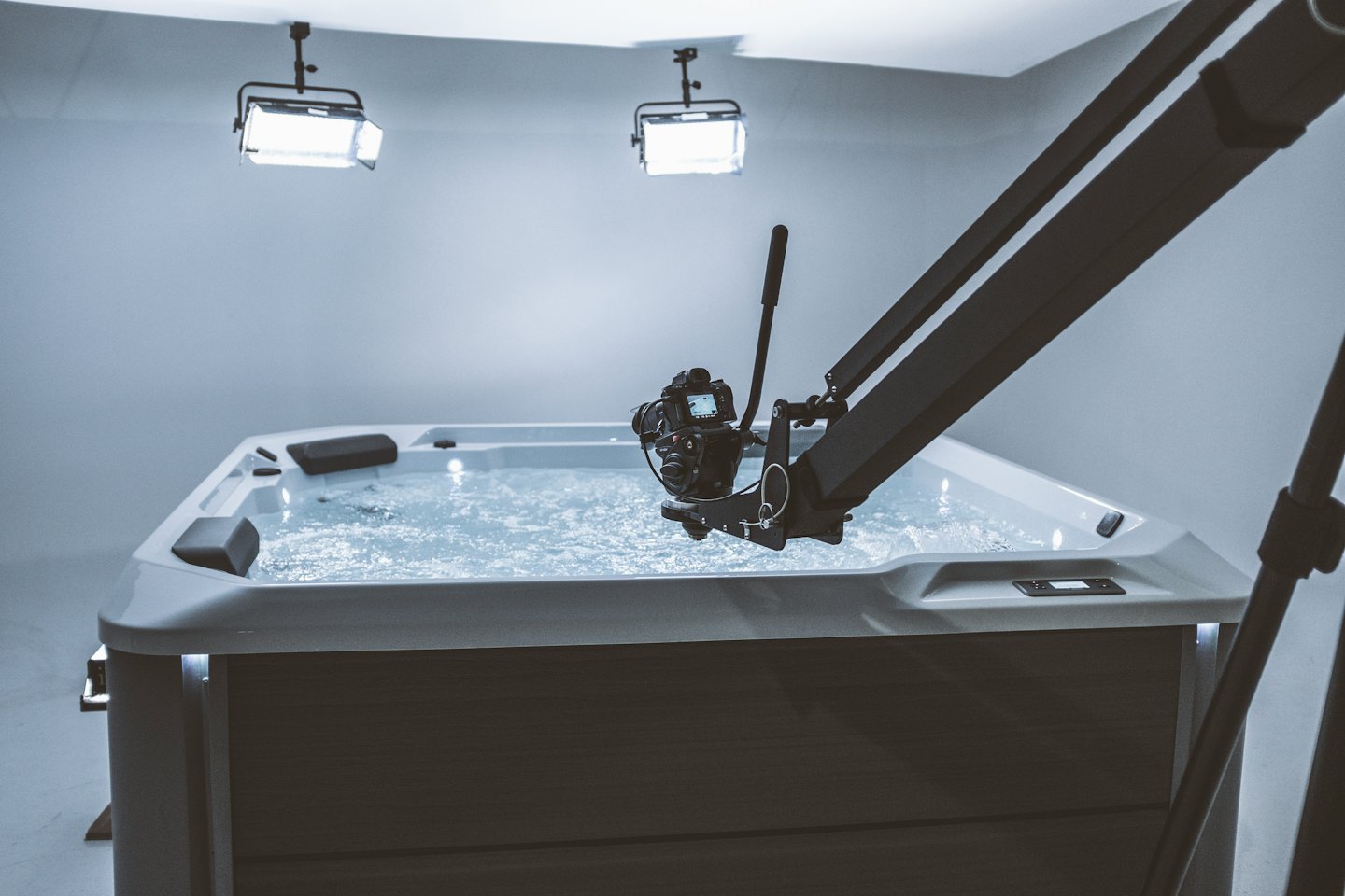 A professional camera films a dark grey hot tub in a studio.
