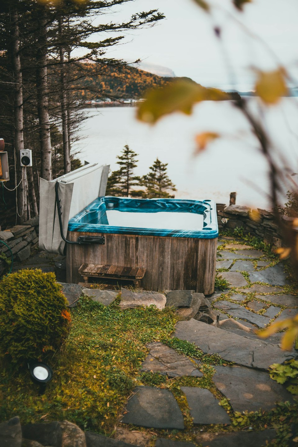 Outdoor hot tub on a flagstone path near evergreen trees.